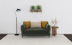 a green couch sitting on top of a white rug next to a lamp and table