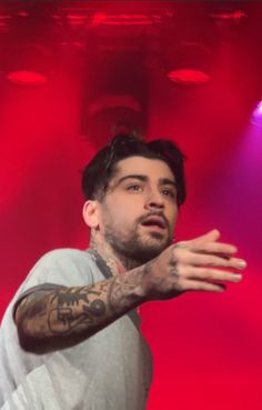 a man with tattoos on his arm and chest standing in front of red lights holding his hands out to the side