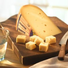 a wooden cutting board topped with cheese next to a glass of water and a knife