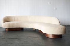 a curved couch sitting on top of a wooden floor next to a white painted wall