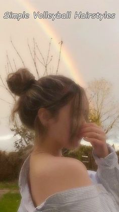 a woman standing in front of a rainbow with her hair pulled back into a bun