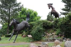 two statues of horses are on display in the grass next to some rocks and trees