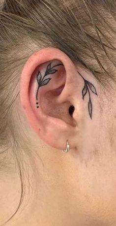 a woman's ear has a small leaf tattoo on it