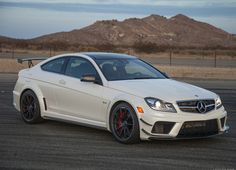 a white mercedes cla is parked in an empty lot with mountains in the background