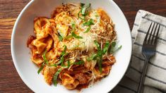 a white bowl filled with pasta and sauce on top of a wooden table next to a fork