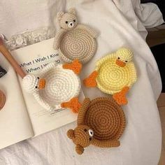 four crocheted ducks sitting on top of a bed next to an open book