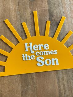 here comes the son cut out from yellow paper on wooden table with sunburst