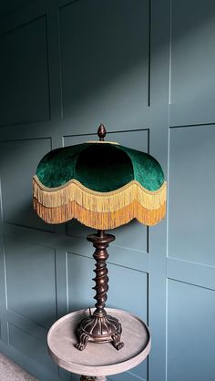 a table lamp with a green and gold shade on it's base, against a blue wall