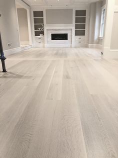 an empty living room with white walls and wood flooring in the center is a fireplace