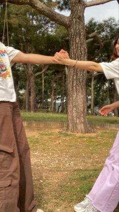 two people holding hands while standing in front of a tree with their arms stretched out