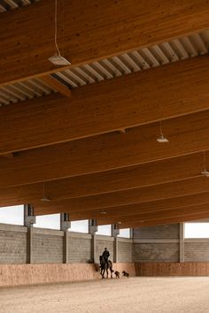 two people are walking their dogs in an enclosed area with wooden beams on the ceiling