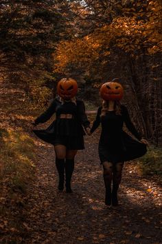 two women dressed in halloween costumes walking down a path with pumpkins on their heads