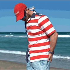 a man wearing a red, white and blue striped shirt standing on the beach next to the ocean