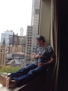 a man sitting on a window sill with his feet propped up against the glass