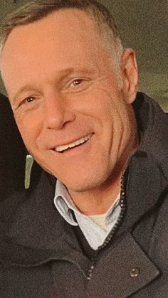 a close up of a person wearing a jacket and smiling at the camera while sitting in a car