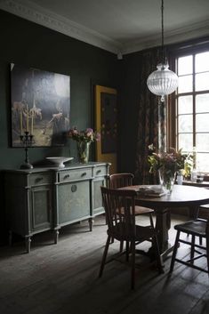 a dining room table and chairs in front of a window with an art work on the wall