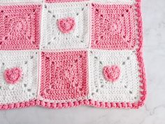 a pink and white crocheted square with hearts on it sitting on a table