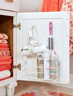 an organized bathroom cabinet with pink towels and hairdryers on the door, along with other personal care items