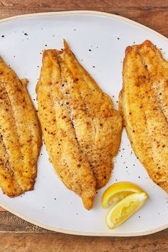 three fish fillets on a plate with lemon wedges and the words best baked catfish