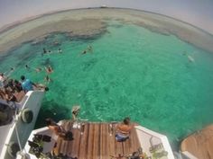 people are swimming in the clear blue water on a boat that's docked at an island