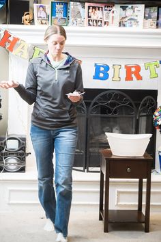 a woman is walking in front of a birthday banner and fireplace with her hands out