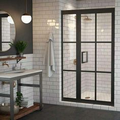 a white tiled bathroom with black trim and glass shower door, sink and mirror on the wall