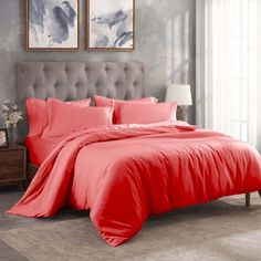 a bed with red comforter and pillows in a gray room next to a window