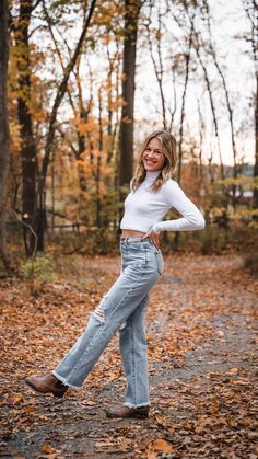 a woman standing in the leaves with her hands on her hips and looking at the camera