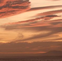 an orange and pink sunset over the ocean with clouds in the sky as seen from a beach