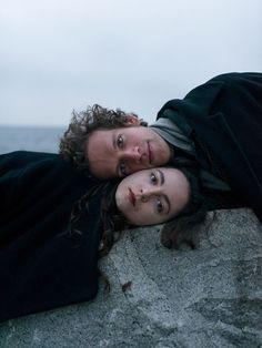 two people laying on top of a rock next to the ocean with their eyes closed