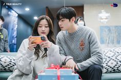 two people sitting on a couch looking at a cell phone with a gift in front of them