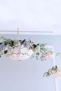 flowers and greenery are hanging from a chandelier in a white walled room