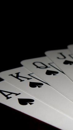 four playing cards are arranged in the shape of spades on a black table top