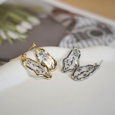 two pairs of butterfly shaped earrings sitting on top of a white plate with flowers in the background