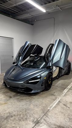 a grey sports car parked in a garage with its doors open and the hood up