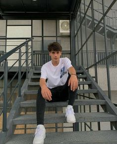 a young man sitting on top of a set of stairs next to a metal hand rail