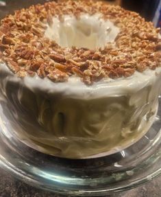 a cake with white frosting and walnuts on top sitting on a glass plate