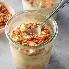 two glass jars filled with food sitting on top of a gray counter next to a bowl of granola