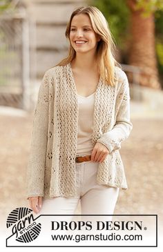 a woman in white pants and a cardigan smiles at the camera while standing outside