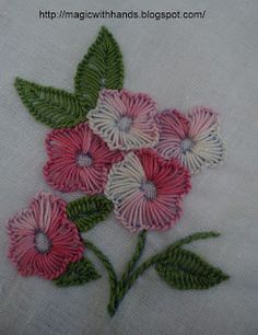 some pink flowers and green leaves on a white table cloth with stitching work in the middle