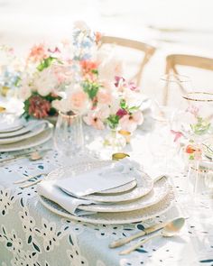 the table is set with white plates and silverware, pink flowers in vases