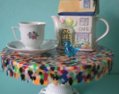 there is a tea cup and saucer on the table with a doll house next to it