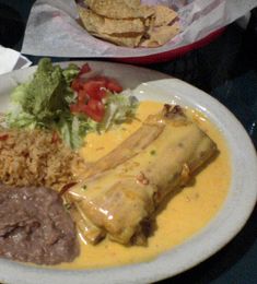 mexican food on a plate with rice, beans and tortilla bread in the background