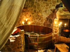 an old fashioned hot tub in a stone walled room with candles on the walls and wood floors