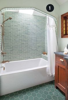 a bathroom with green tiled walls and flooring, including a white bathtub next to a wooden cabinet