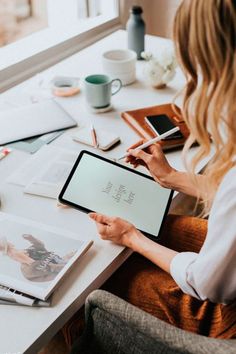 a woman sitting at a table with a tablet computer and papers on top of it