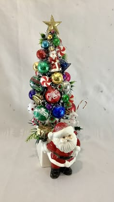 a small christmas tree with ornaments on it's base and a santa clause figurine next to it