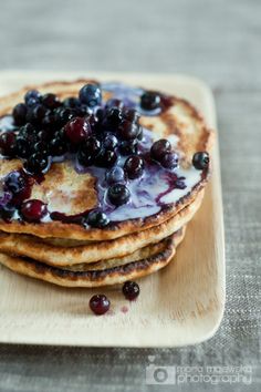 pancakes with blueberries and syrup are on a wooden plate, ready to be eaten