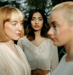 three women standing next to each other with makeup on their faces and one wearing a white top