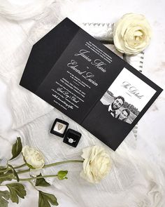 an open black and white wedding card with two roses on the table next to it